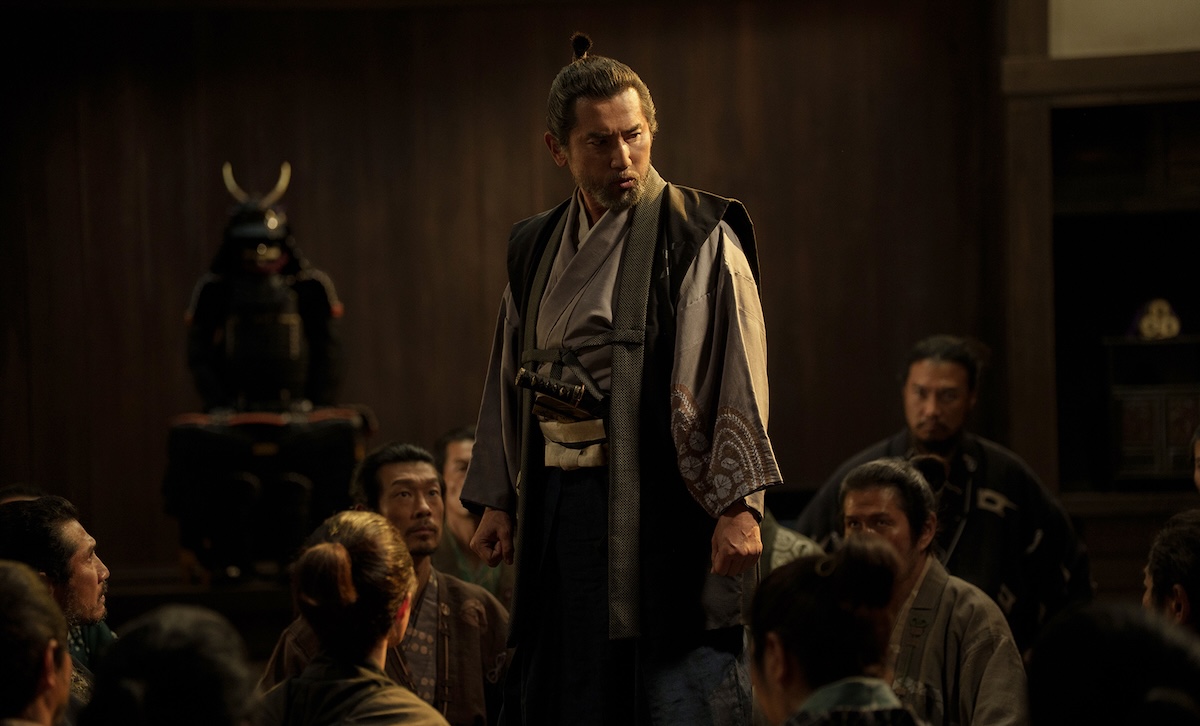The Samurai and the Prisoner theatrical production scene featuring a samurai standing amidst seated characters in historical Japanese attire.